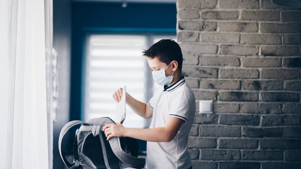 Quarantined child packing his books to school backpack.